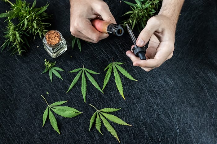 Cannabis liquid. Vape CBD or THC, Vaping Marijuana Leaves and Hemp. On a dark background. Hands run the vape.