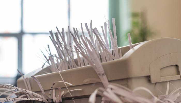 A compact office paper shredder with white paper going through the blade. The paper is shredded in strips.