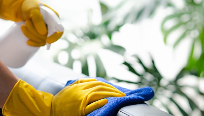 A person wearing yellow cleaning gloves sprays a substance onto a leather surface and wipes it clean with a blue cloth.