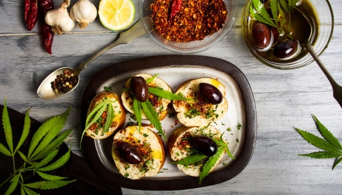A table with restaurant food, loose spices, and other ingredients. The plate with food has cannabis leaves as garnishment.