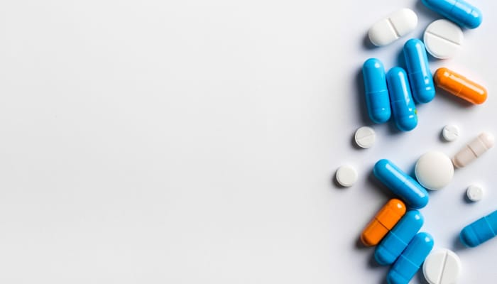 A variety of blue, orange, and white pills are scattered across a white background to the right side.