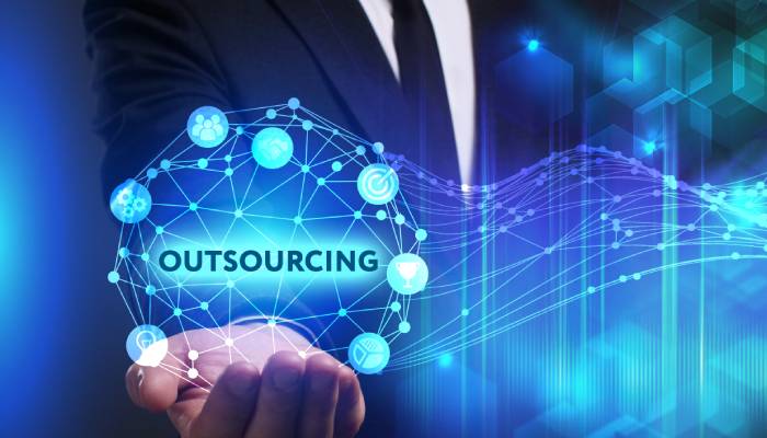 A businessman extending his hand to cup a floating digital design of connected dots and the word "outsourcing."