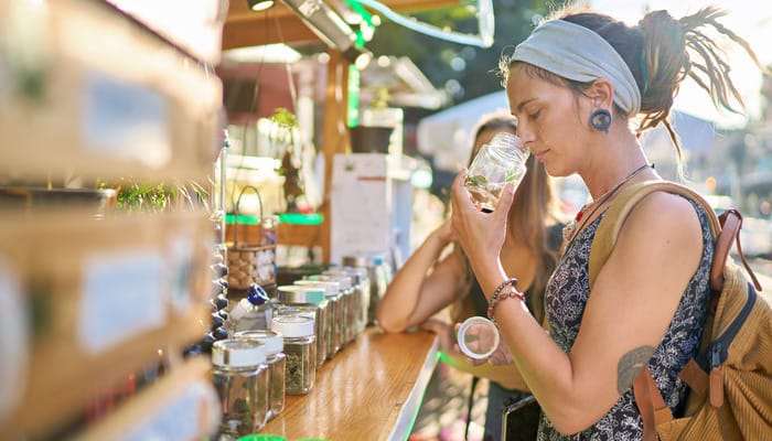 Two females at a cannabis fair booth smelling cannabis flower in glass jars. There's a row of sample jars on the counter.