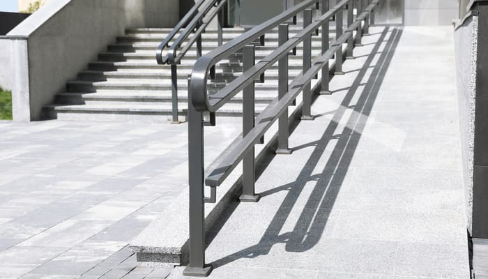 A ramp and staircase appear outside of a gray commercial building. Metal railings are next to the staircase and ramp.