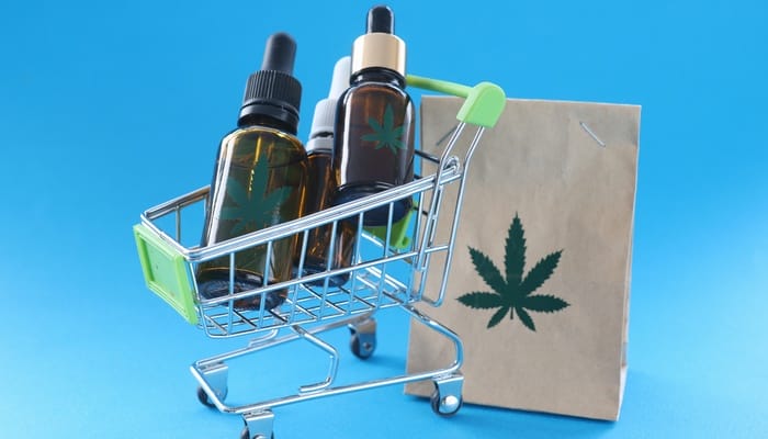 A brown paper bag with a marijuana plant on it next to a grocery cart filled with bottles with marijuana plants on them.