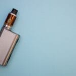 A metal vape pen lies on a blue background, showcasing sleek design and modern electronic cigarette style.