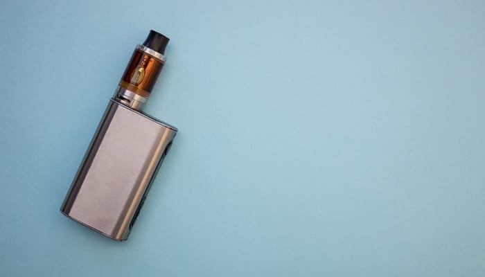 A metal vape pen lies on a blue background, showcasing sleek design and modern electronic cigarette style.