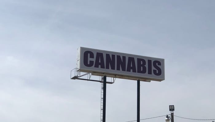 A large directional billboard elevated at a height, displaying the word "cannabis" in big, bold letters.