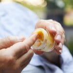 A person holding a small container of CBD cream. They are running their fingers through the half-empty jar.