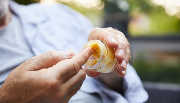 A person holding a small container of CBD cream. They are running their fingers through the half-empty jar.