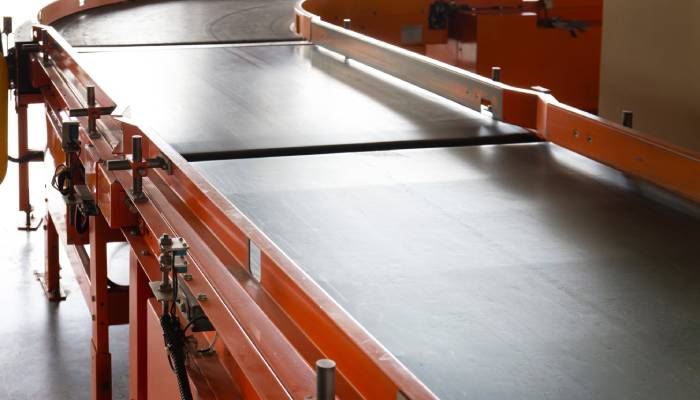 A conveyor system with a rubber belt moves around the corner of a facility. The system has a red framework.
