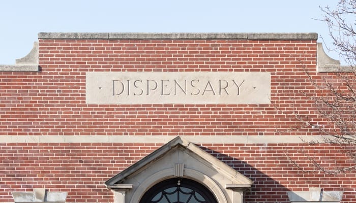 A red brick building contains a concrete sign built into the brick that reads "dispensary." The building has three windows.