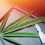 A car key and a marijuana leaf resting on the center console of a vehicle, illuminated by bright orange light.