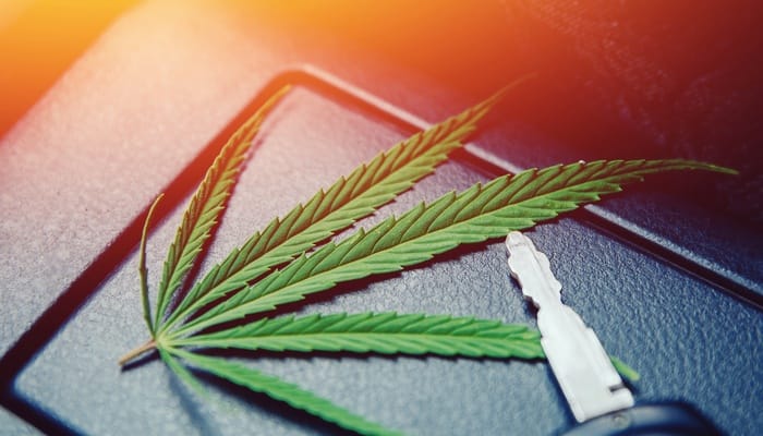 A car key and a marijuana leaf resting on the center console of a vehicle, illuminated by bright orange light.
