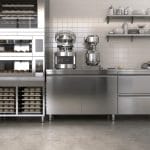 A kitchen contains modern stainless steel appliances, including mixers, ovens, freezers, scales and more.