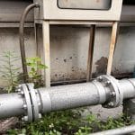 A section of pipeline running outside. There is a flexible section of the pipeline holding the two metal parts together.