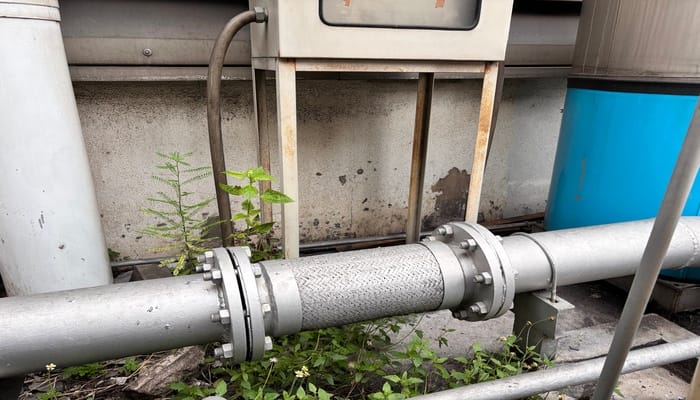 A section of pipeline running outside. There is a flexible section of the pipeline holding the two metal parts together.