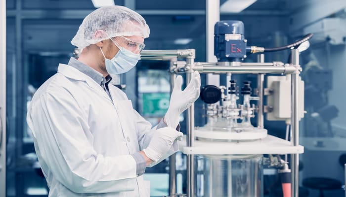 A scientist putting on rubber gloves. He is standing next to a hemp oil extraction machine that has a lot of metal parts.