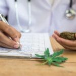 A close-up of a person in a white lab coat writing notes on a clipboard while holding a cannabis sample.