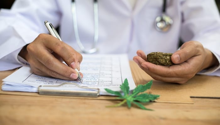 A close-up of a person in a white lab coat writing notes on a clipboard while holding a cannabis sample.
